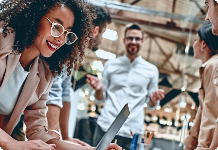 A group of people in a warehouse setting with one of the people smiling while working on her laptop.