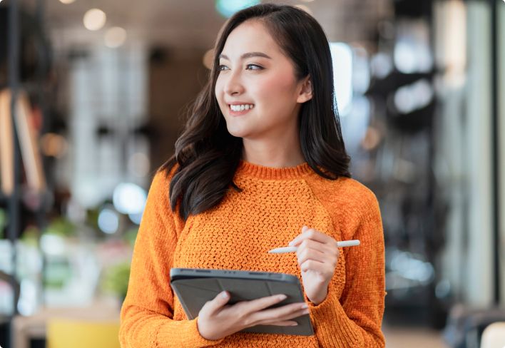 Happy young woman standing in a furniture store taking stock on an iPad 