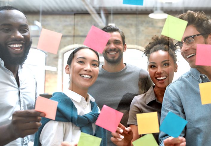 A group of co-workers placing colored sticky notes on a clear board.