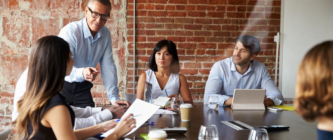 Professional people at a desk taking instruction in a meeting room