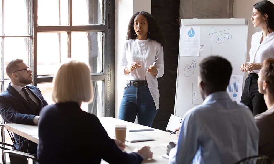 Adult professionals watching a teacher doing instructions on a whiteboard in an office setting