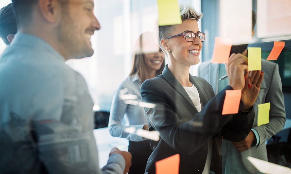 Group of co-workers brainstorming ideas on post-it notes on a glass wall