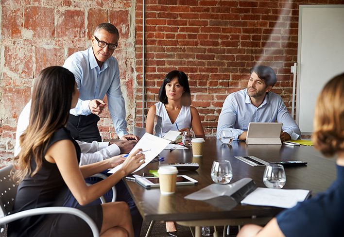 Professional people at a desk taking instruction in a meeting room