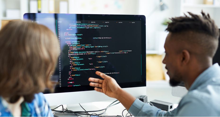 Two employees reviewing some code on a monitor