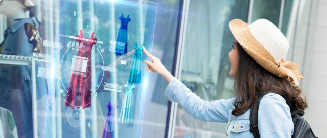  A young woman is touching the glass of a store window upon which we see several computer-generated images of dresses in different colors. 