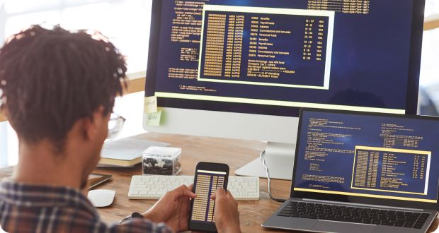 Young developer reviewing code on a desktop, laptop, and mobile device